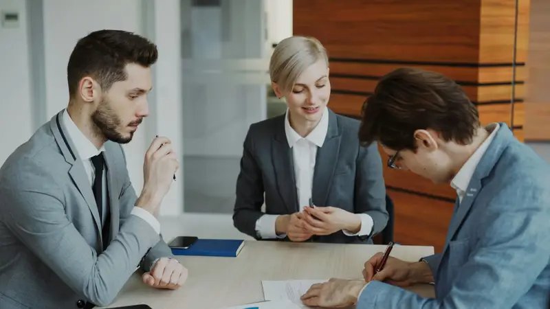 Anwältin im Gespräch mit zwei Mandanten an einem hellen Besprechungstisch