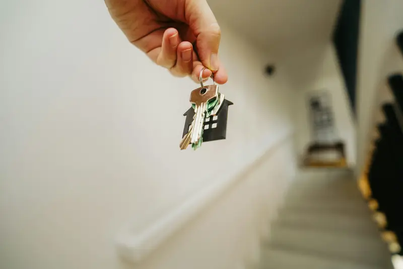 Hand hält einen Wohnungsschlüssel in einem hellen Treppenhaus