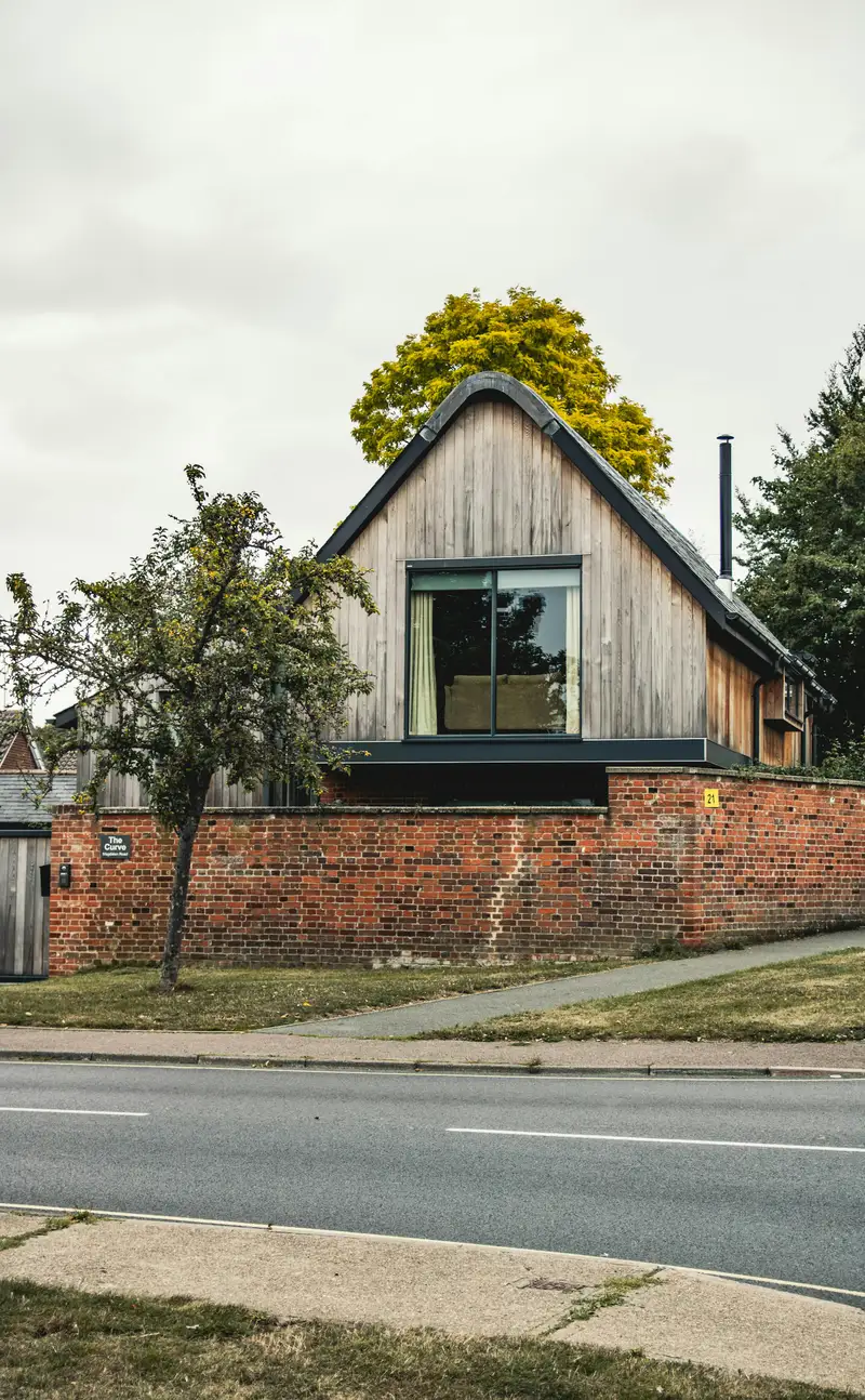 Holzverkleidetes Giebelhaus mit großem Fenster hinter einer Ziegelmauer