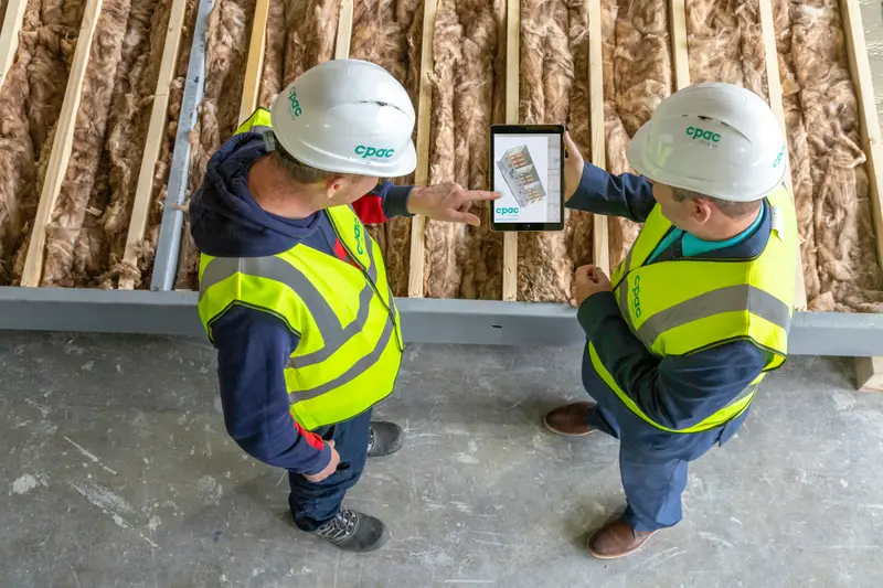 Zwei Personen in Warnwesten prüfen Pläne auf einem Tablet auf der Baustelle
