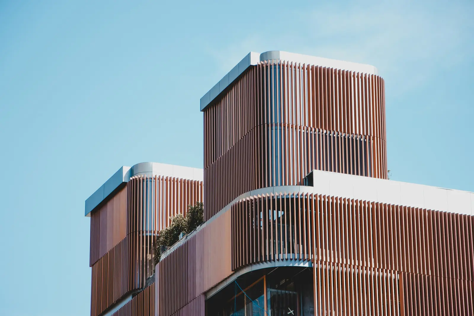Gebäude mit runden Ecken und senkrechten Holzlamellen vor blauem Himmel
