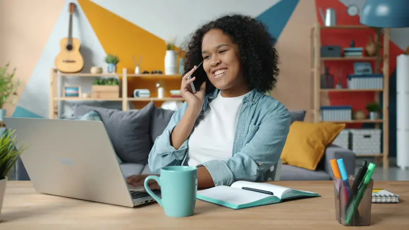 Frau telefoniert am Schreibtisch und arbeitet dabei am Laptop