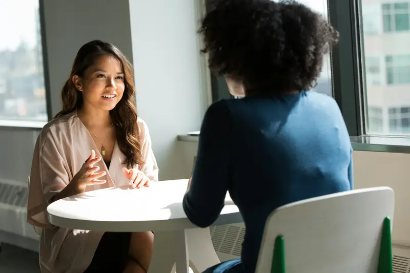 Zwei Frauen sitzen sich am runden Tisch gegenüber und sprechen