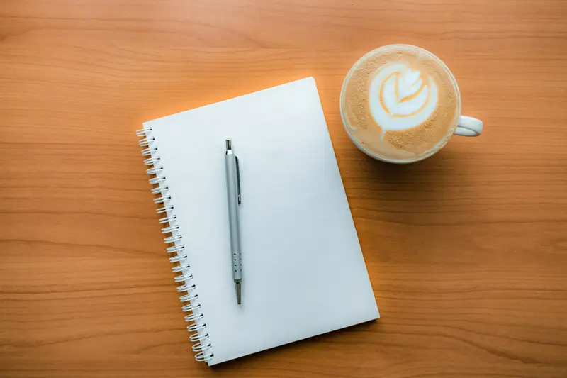 Notizbuch mit Stift neben einer Tasse Kaffee auf Holz