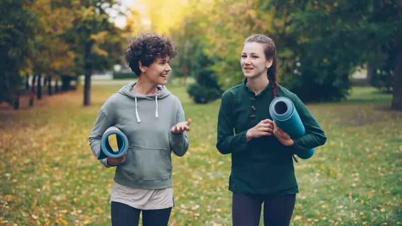 Zwei Frauen gehen im Gespräch durch einen herbstlichen Park