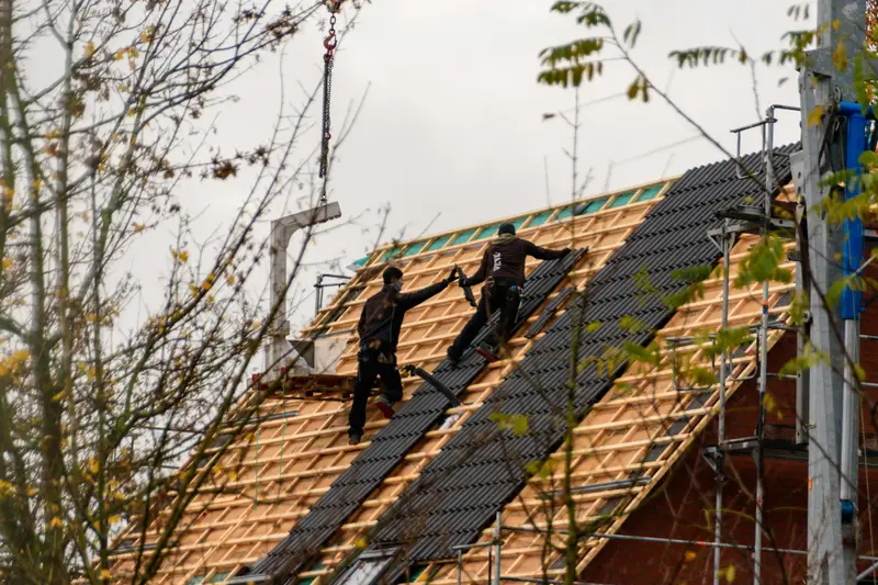 Dachdecker-Team bei der Arbeit auf einem Steildach, Material kommt per Kran