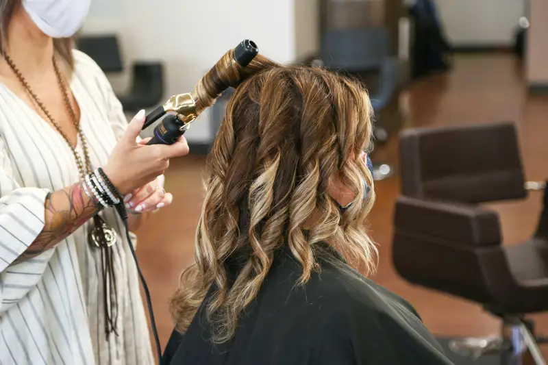 Friseurin formt mit dem Lockenstab Wellen in Haar mit Balayage