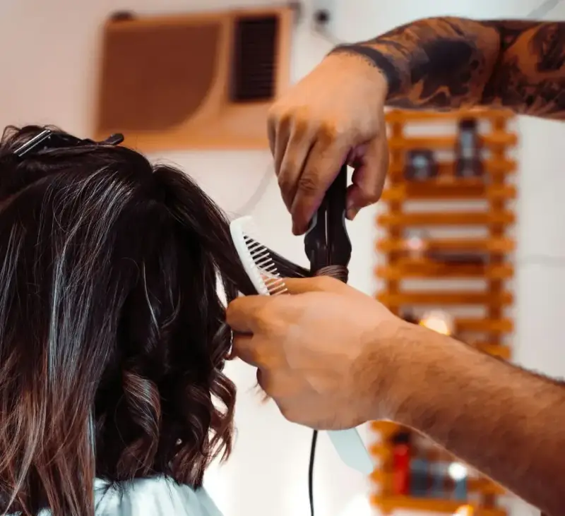 Friseur schneidet dunkelbraunes, schulterlanges Haar mit Kamm und Schere