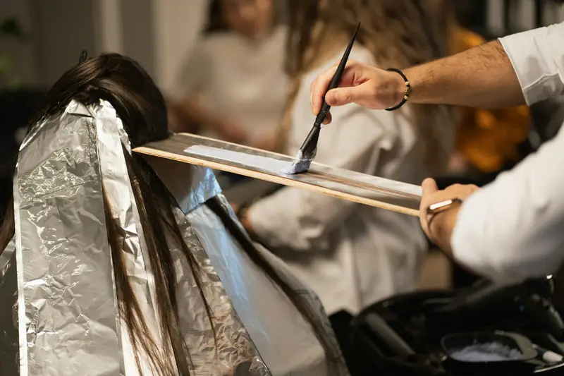 Coloristin trägt Farbe mit dem Pinsel auf Strähnen in Folie auf