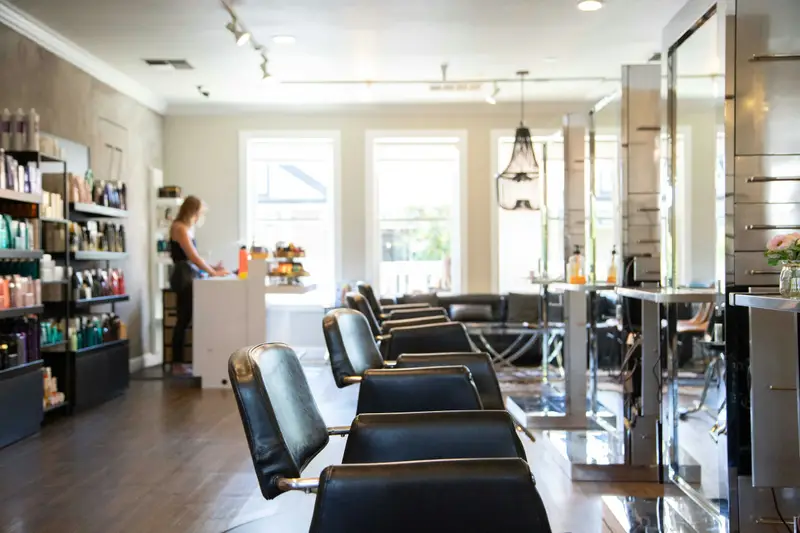 Heller Salon mit einer Reihe schwarzer Friseurstühle und großen Fenstern