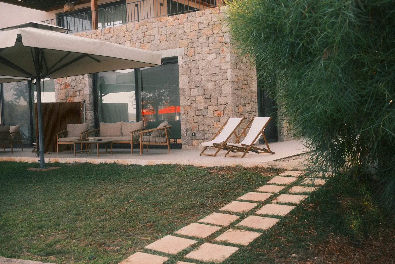 Neu angelegter Garten an einem Haus mit Natursteinfassade: Terrasse, Rasen und Trittplattenweg