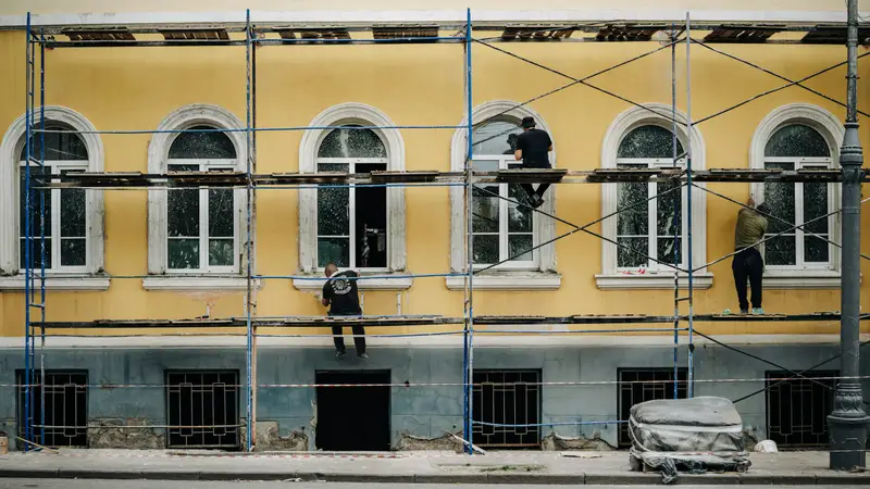 Maler auf dem Gerüst vor einer ockergelben Altbaufassade mit Rundbogenfenstern