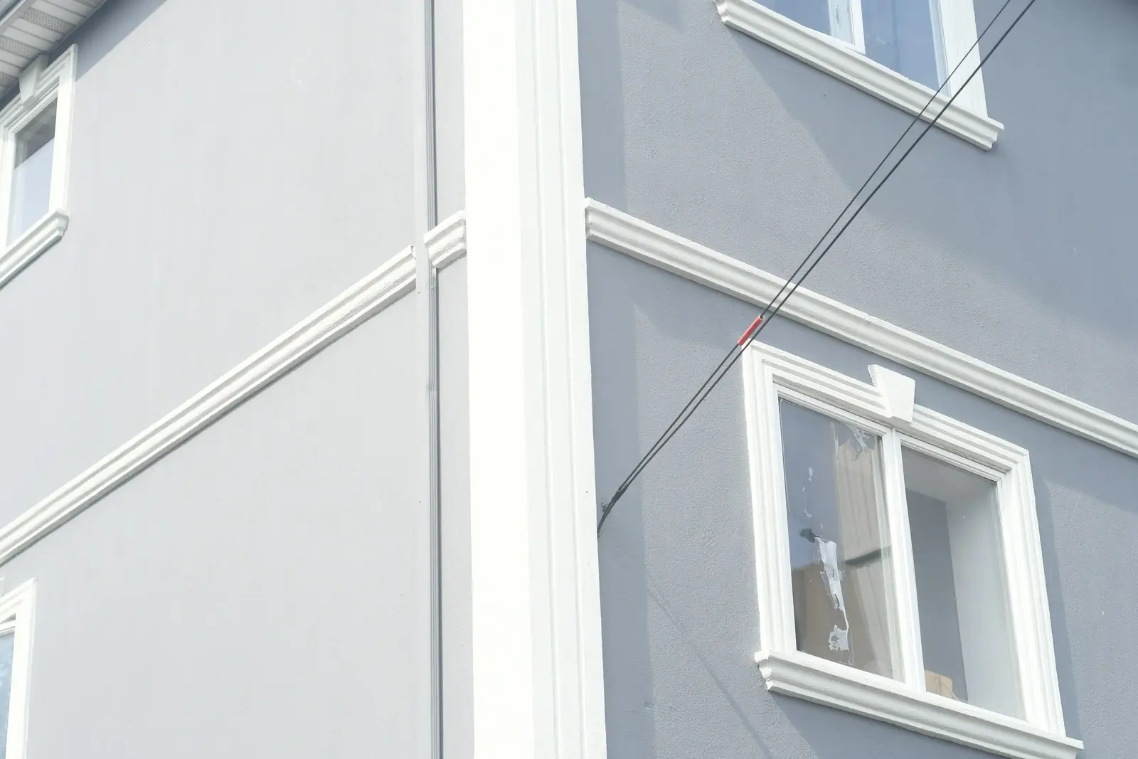 Hellgraue Putzfassade mit weiß abgesetzten Fensterfaschen