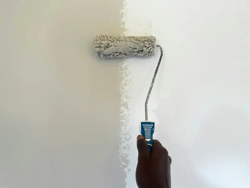 Farbrolle streicht eine graue Wand weiß