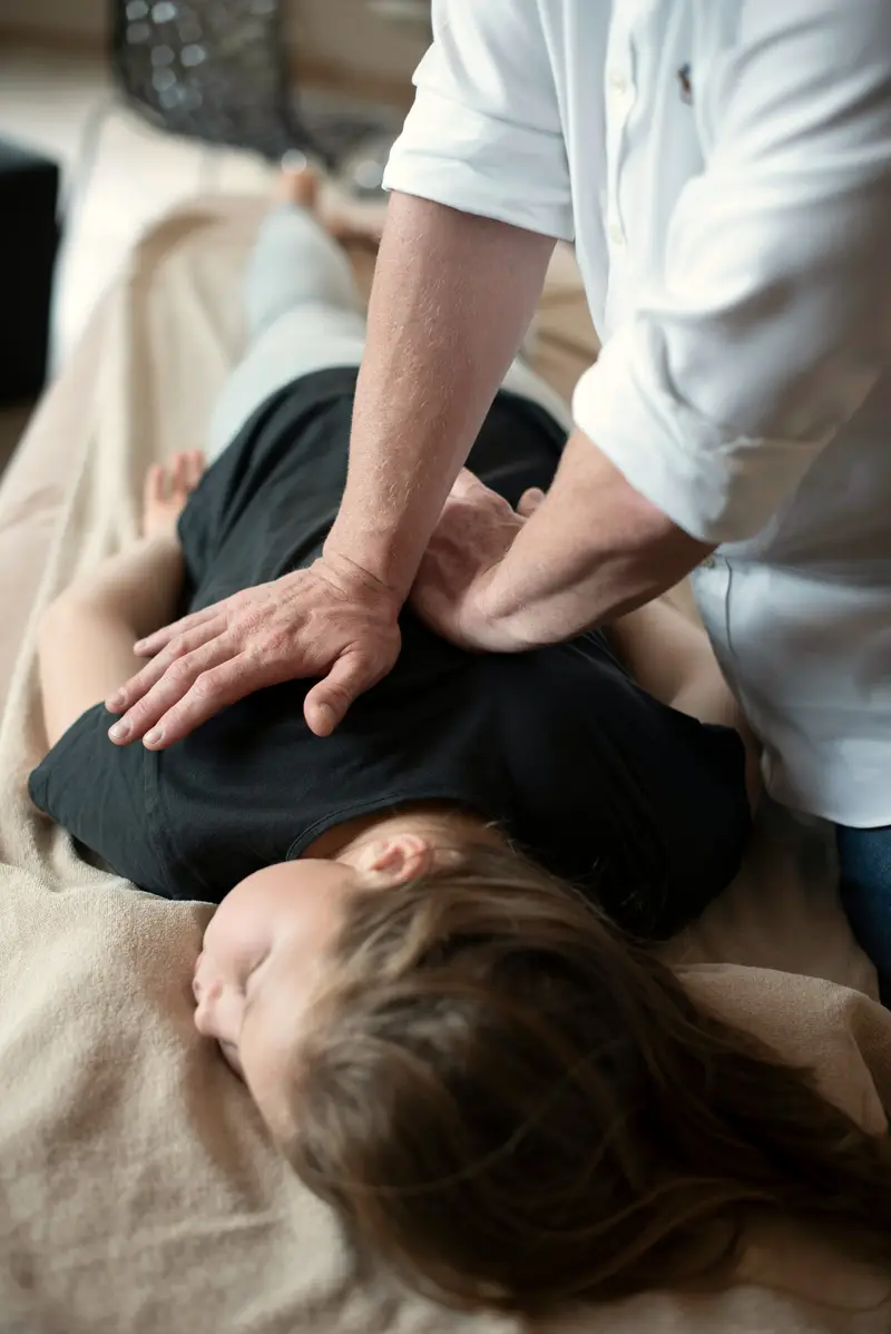 Hände eines Therapeuten bei der Behandlung am oberen Rücken einer Patientin