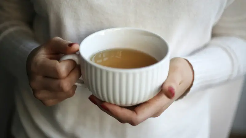Zwei Hände halten eine weiße Teetasse